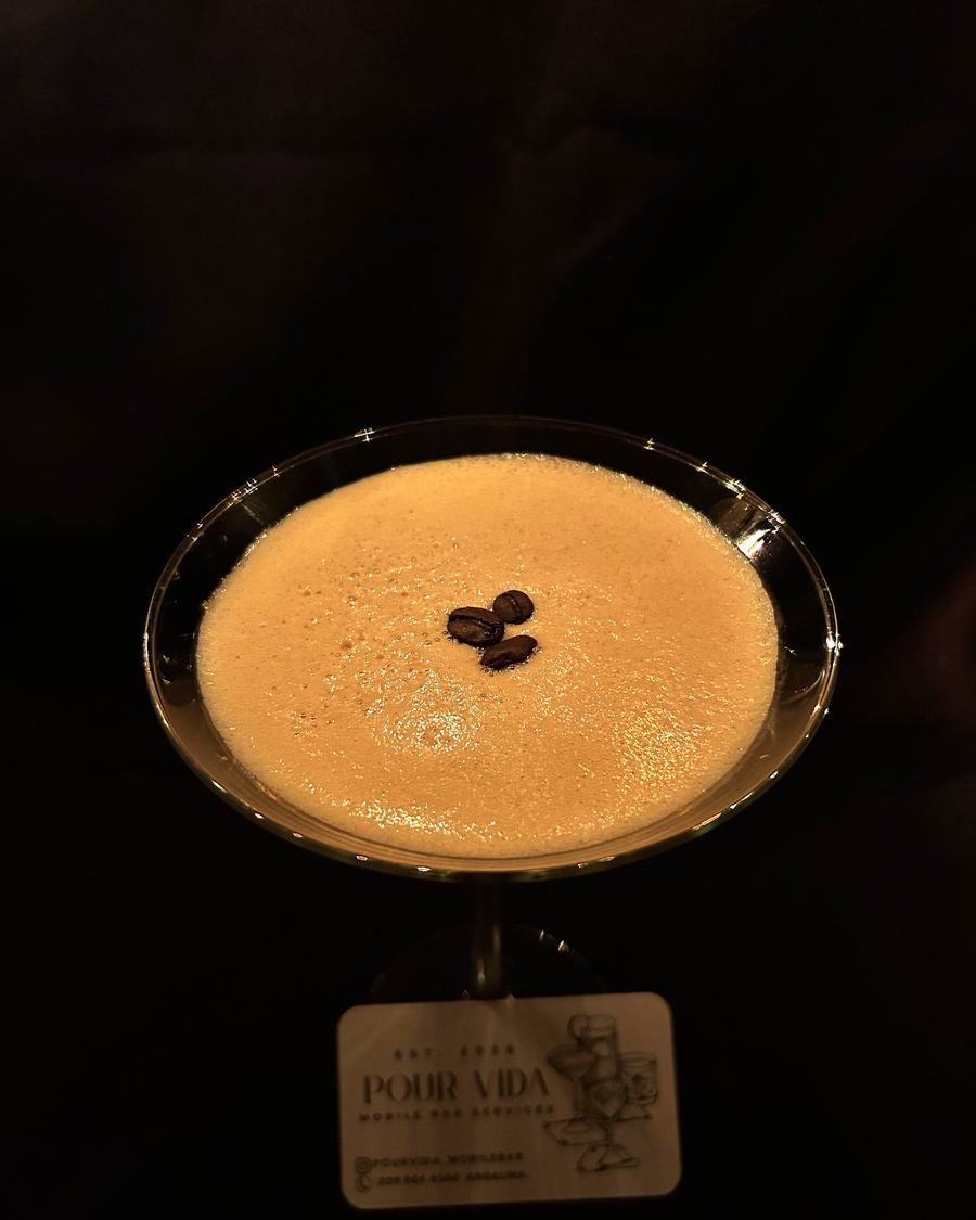 Espresso martini with a foam top and three coffee beans, a Pour Vida business card in front