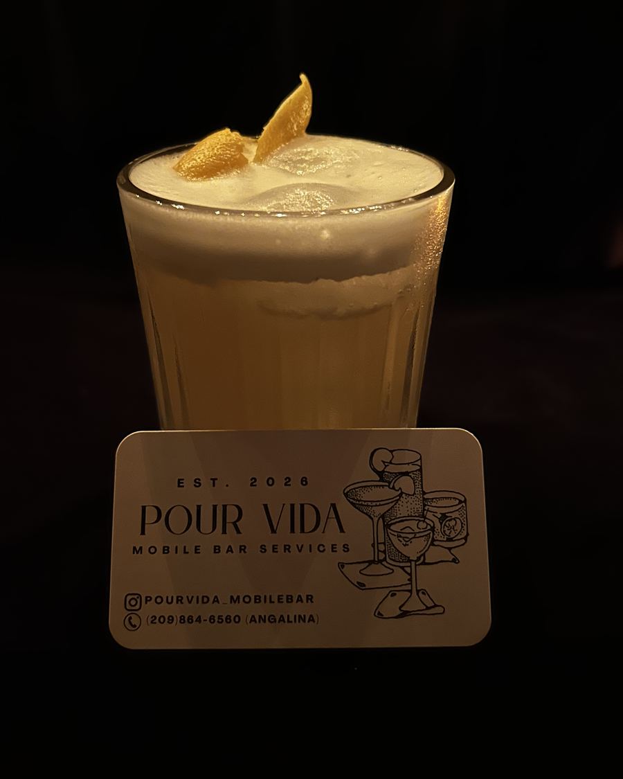 Whisky sour in a ribbed glass behind a Pour Vida Mobile Bar Services business card